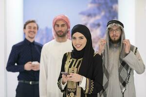 Group portrait of young Muslim people women in fashionable hijab dress with three Arabian men using smartphones at modern bright home photo