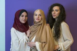 Group portrait of beautiful Muslim women two of them in a fashionable dress with hijab isolated on a colorful background photo