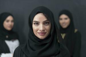 Group portrait of beautiful Muslim women in a fashionable dress with hijab isolated on black background photo