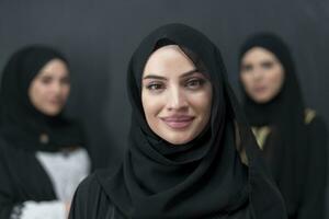 Group portrait of beautiful Muslim women in a fashionable dress with hijab isolated on black background photo