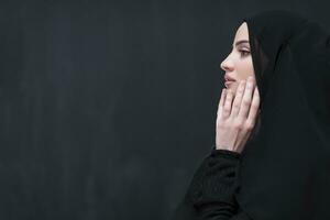 Portrait of beautiful muslim woman in fashionable dress with hijab making traditional prayer to God keeps hands in praying gesture isolated on black background photo