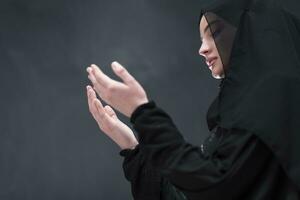 retrato de hermosa musulmán mujer en de moda vestir con hijab haciendo tradicional oración a Dios mantiene manos en Orando gesto aislado en negro antecedentes foto