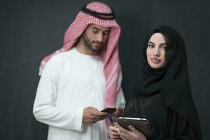 Young muslim business couple in fashionable hijab dress using smartphone and tablet in front of black background photo