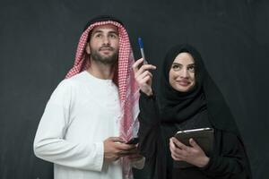 Young muslim business couple in fashionable hijab dress using smartphone and tablet in front of black background photo