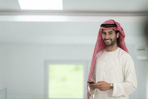 Young modern Muslim Arabian businessmen wearing traditional clothes while using smartphones at home. High-quality photo