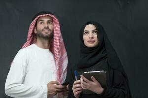 Young muslim business couple in fashionable hijab dress using smartphone and tablet in front of black background photo