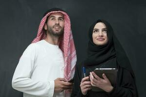 Young muslim business couple in fashionable hijab dress using smartphone and tablet in front of black background photo