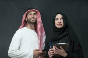 Young muslim business couple in fashionable hijab dress using smartphone and tablet in front of black background photo