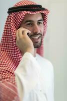 Young modern Muslim Arabian businessmen wearing traditional clothes while using smartphones at home. High-quality photo