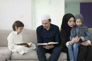 tradicional musulmán familia padres con niños leyendo Corán y Orando juntos en el sofá antes de iftar cena durante un Ramadán banquete a hogar foto