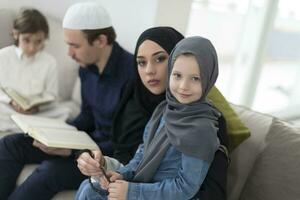 tradicional musulmán familia padres con niños leyendo Corán y Orando juntos en el sofá antes de iftar cena durante un Ramadán banquete a hogar foto