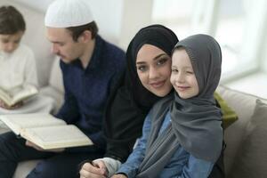 Traditional muslim family parents with children reading Quran and praying together on the sofa before iftar dinner during a ramadan feast at home photo