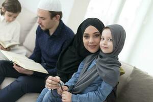 Traditional muslim family parents with children reading Quran and praying together on the sofa before iftar dinner during a ramadan feast at home photo