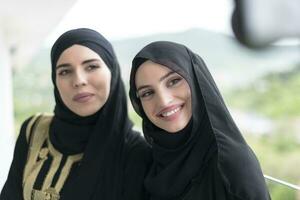 young beautiful muslim women in fashionable dress with hijab using mobile phone while taking selfie picture on the balcony representing modern islam fashion technology and ramadan kareem concept photo