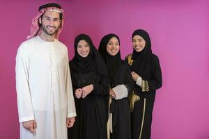 Group portrait of young Muslim people Arabian men with three Muslim women in a fashionable dress with hijab isolated on a pink background photo