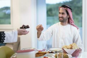 moderno multiétnico musulmán familia compartiendo un cuenco de fechas mientras disfrutando iftar cena juntos durante un Ramadán banquete a hogar foto