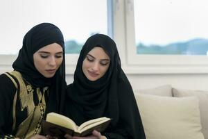 joven tradicional musulmán mujer leer Corán en el sofá antes de iftar cena durante un Ramadán banquete a hogar. foto