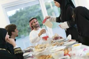 eid Mubarak musulmán familia teniendo iftar cena Bebiendo agua a descanso banquete. comiendo tradicional comida durante Ramadán banquete mes a hogar. el islámico halal comiendo y Bebiendo a moderno occidental isla foto