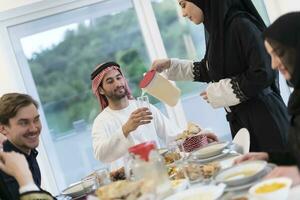 eid Mubarak musulmán familia teniendo iftar cena Bebiendo agua a descanso banquete. comiendo tradicional comida durante Ramadán banquete mes a hogar. el islámico halal comiendo y Bebiendo a moderno occidental isla foto