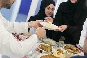 eid Mubarak musulmán familia teniendo iftar cena Bebiendo agua a descanso banquete. comiendo tradicional comida durante Ramadán banquete mes a hogar. el islámico halal comiendo y Bebiendo a moderno occidental isla foto