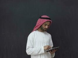 young arabian muslim businessman using tablet computer wearing hijab clothes in front of black chalkboard photo