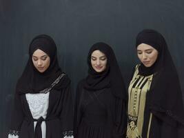 Group portrait of beautiful Muslim women in a fashionable dress with hijab isolated on black background photo