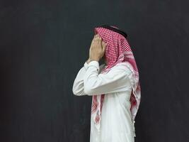 A young Arabian man in traditional clothes making a traditional prayer to God keeps his hands in praying gesture in front of a black background photo