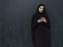 Young modern muslim business woman using smartphone wearing hijab clothes in front of black chalkboard photo