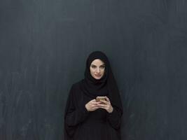 Young modern muslim business woman using smartphone wearing hijab clothes in front of black chalkboard photo