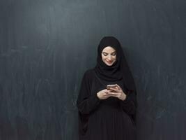 Young modern muslim business woman using smartphone wearing hijab clothes in front of black chalkboard photo