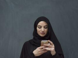 Young modern muslim business woman using smartphone wearing hijab clothes in front of black chalkboard photo