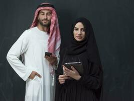 Young muslim business couple in fashionable hijab dress using smartphone and tablet in front of black background photo