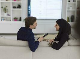 Young muslim couple woman wearing islamic hijab clothes sitting on sofa watching TV together during the month of Ramadan at modern home photo