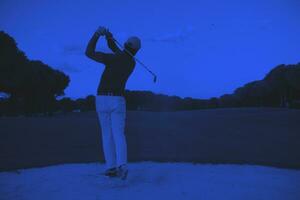 golfer hitting a sand bunker shot on sunset photo