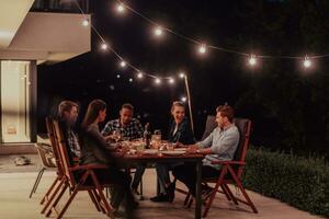 A group of young diverse people having dinner on the terrace of a modern house in the evening. Fun for friends and family. Celebration of holidays, weddings with barbecue. photo