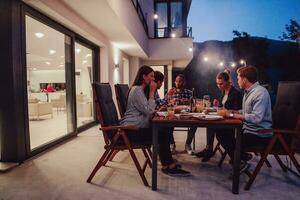 A group of young diverse people having dinner on the terrace of a modern house in the evening. Fun for friends and family. Celebration of holidays, weddings with barbecue. photo