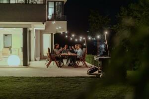 A group of young diverse people having dinner on the terrace of a modern house in the evening. Fun for friends and family. Celebration of holidays, weddings with barbecue. photo