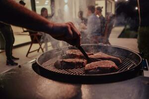 Close-up photo of delicious meat being grilled. In the background, friends and family are sitting and waiting for a meal