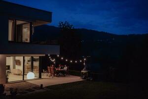 un grupo de joven diverso personas teniendo cena en el terraza de un moderno casa en el noche. divertido para amigos y familia. celebracion de vacaciones, bodas con parilla. foto