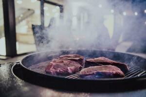 Close-up photo of delicious meat being grilled. In the background, friends and family are sitting and waiting for a meal