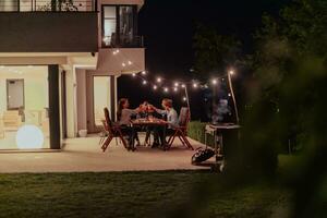 A group of young diverse people having dinner on the terrace of a modern house in the evening. Fun for friends and family. Celebration of holidays, weddings with barbecue. photo