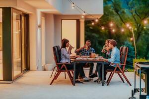 A group of young diverse people having dinner on the terrace of a modern house in the evening. Fun for friends and family. Celebration of holidays, weddings with barbecue. photo
