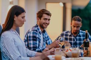 un grupo de joven diverso personas teniendo cena en el terraza de un moderno casa en el noche. divertido para amigos y familia. celebracion de vacaciones, bodas con parilla. foto