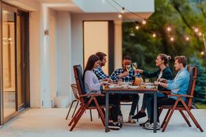 A group of young diverse people having dinner on the terrace of a modern house in the evening. Fun for friends and family. Celebration of holidays, weddings with barbecue. photo
