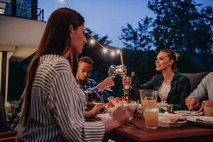 A group of young diverse people having dinner on the terrace of a modern house in the evening. Fun for friends and family. Celebration of holidays, weddings with barbecue. photo