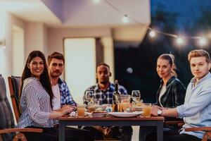 A group of young diverse people having dinner on the terrace of a modern house in the evening. Fun for friends and family. Celebration of holidays, weddings with barbecue. photo