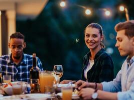 A group of young diverse people having dinner on the terrace of a modern house in the evening. Fun for friends and family. Celebration of holidays, weddings with barbecue. photo