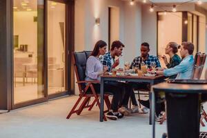 A group of young diverse people having dinner on the terrace of a modern house in the evening. Fun for friends and family. Celebration of holidays, weddings with barbecue. photo