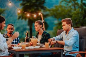 A group of young diverse people having dinner on the terrace of a modern house in the evening. Fun for friends and family. Celebration of holidays, weddings with barbecue. photo