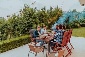 A group of young diverse people having dinner on the terrace of a modern house in the evening. Fun for friends and family. Celebration of holidays, weddings with barbecue. photo